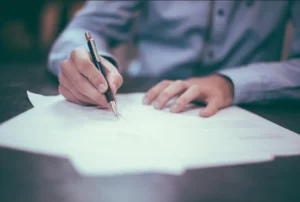 Personne en train de rédiger et signer des formalités administratives sur un bureau.